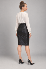 A woman shown from the back wearing a white long-sleeve blouse and a black faux-leather pencil skirt, paired with black high heels, against a solid gray studio background.