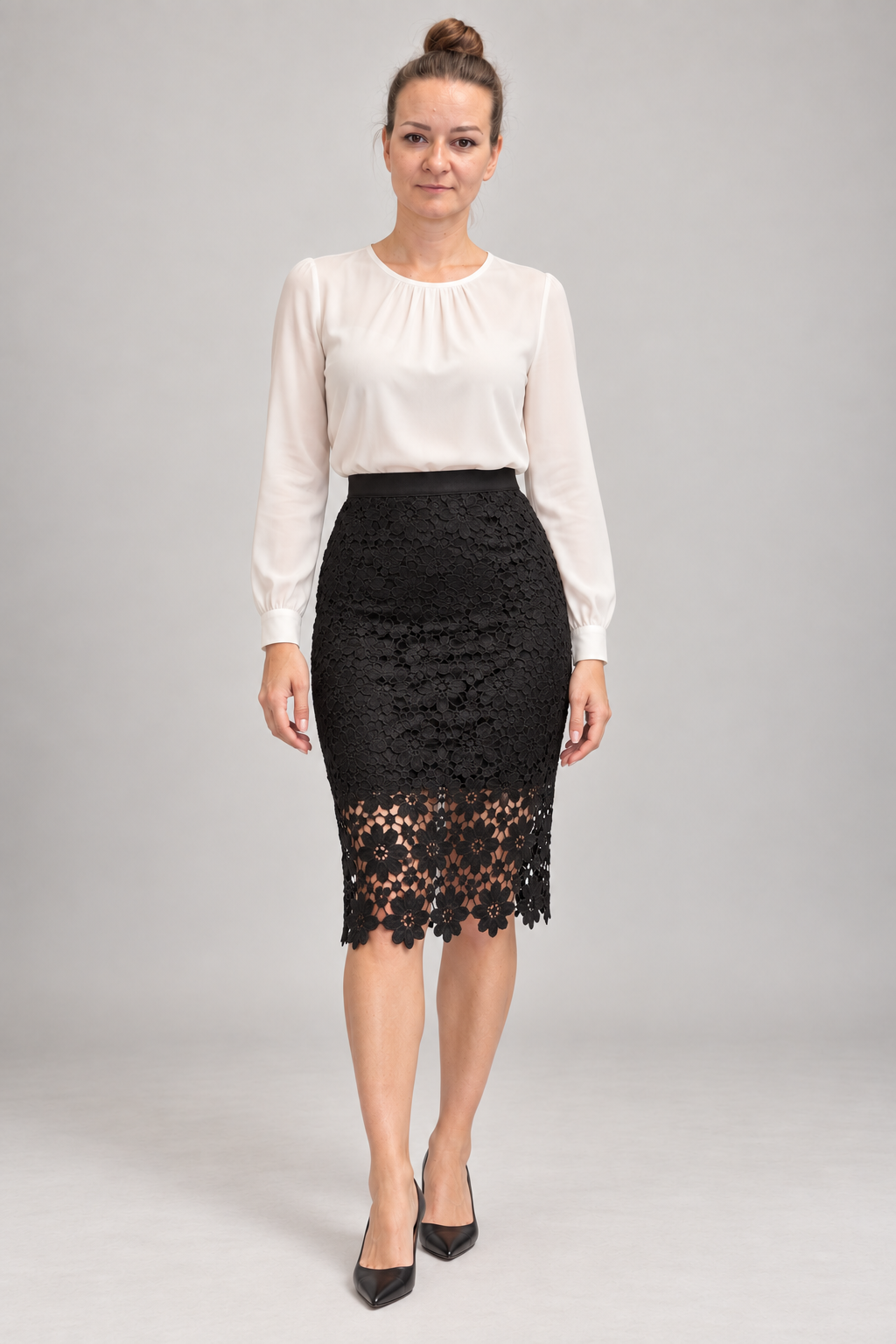 A woman modeling a white long-sleeve blouse and a black lace knee-length skirt against a light gray studio background.