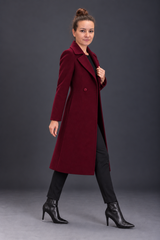 A woman modeling a long burgundy wool-blend coat over a black outfit, standing against a dark gray studio background.