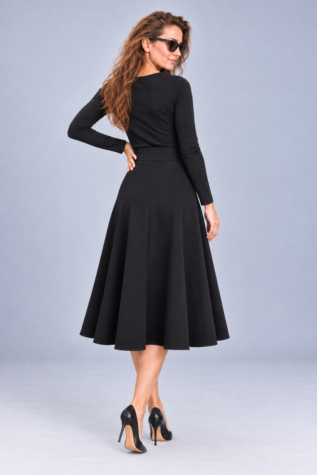 A woman modeling a black long-sleeve midi skirt with a flared A-line silhouette, shown from a rear three-quarter angle against a light gray studio background.