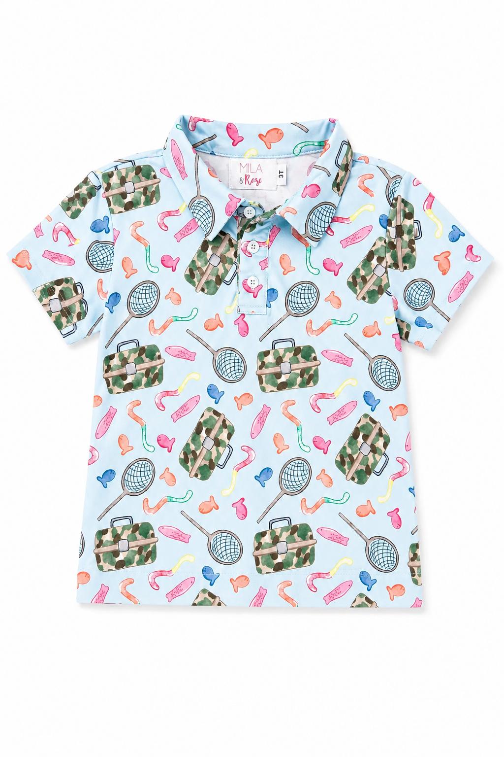 A short-sleeve polo shirt for kids on a white background, featuring a light blue base with a colorful pattern of tennis rackets, bags, and athletic shoes in green camouflage and bright colors.