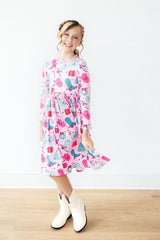 Young girl wearing a colorful dress with a pattern of boots and trees on a white background