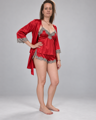 A woman modeling a red satin lingerie set with silver lace trim, consisting of a robe, camisole, and shorts, against a plain gray studio background.