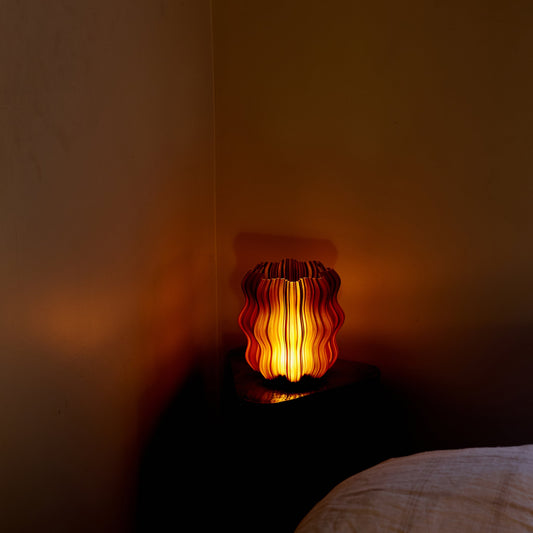Glass lamp with warm glow on a dark surface against a brown wall