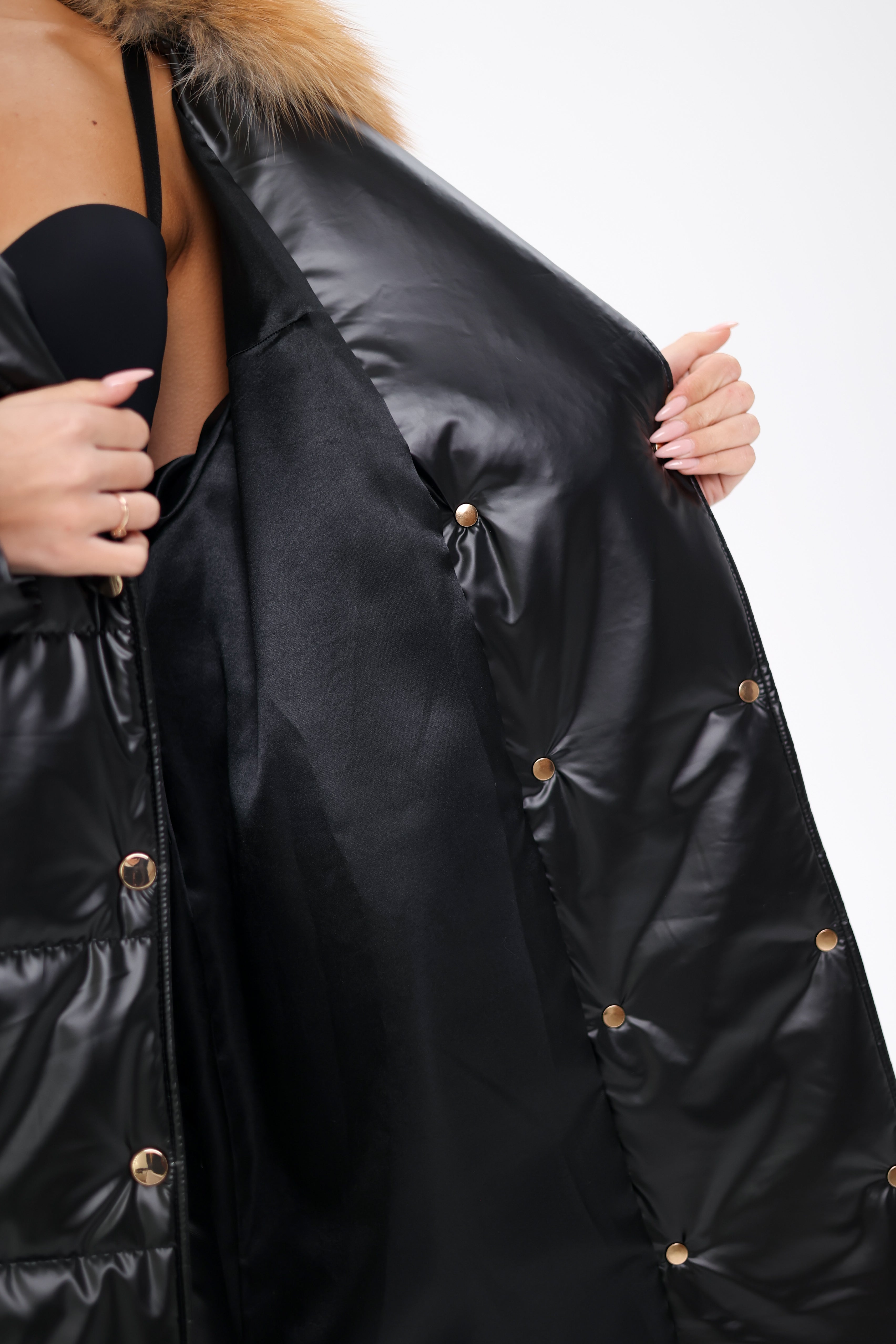 Black puffer jacket with fur hood held open by a person on a white background