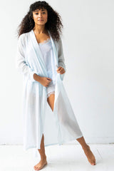 Woman wearing a light blue robe over a white outfit on a white background