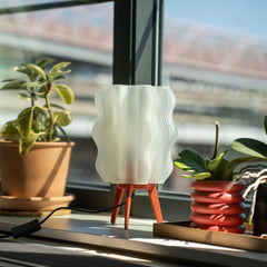 White textured lamp on a windowsill with plants and a blurred outdoor view