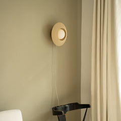 Round wall light fixture on a beige wall with a curtain to the right.