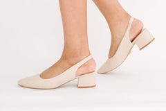 Beige block-heel shoes worn by a person on a white background