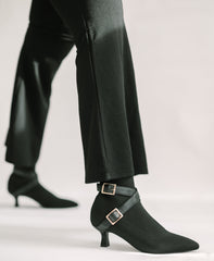Black ankle boots with gold buckles worn with black pants on a light background