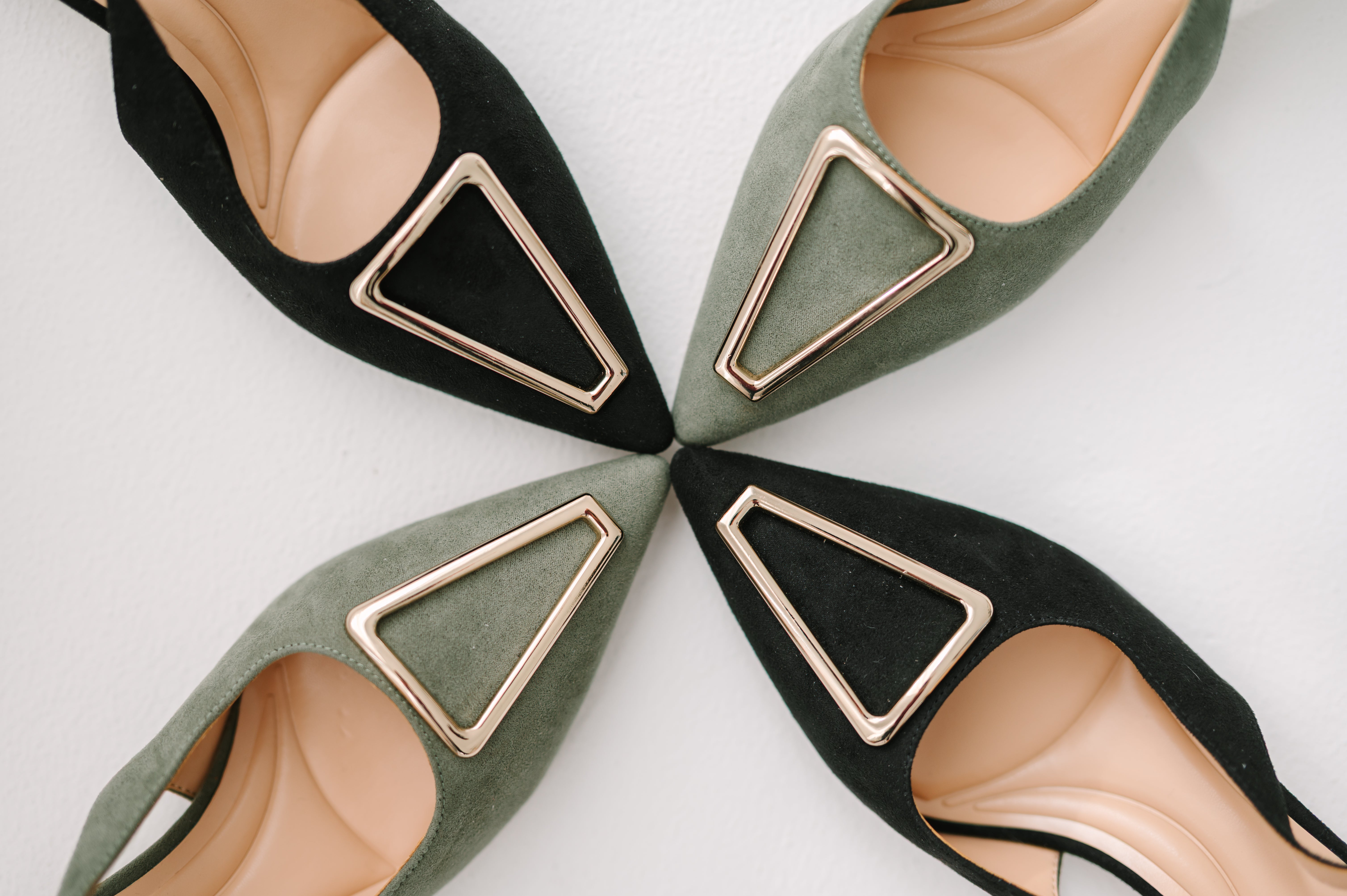 Four pairs of shoes with decorative buckles arranged in a circular pattern on a light background.