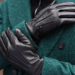 Black leather gloves with contrast stitching, shown worn on a person's hands over a dark green wool coat.