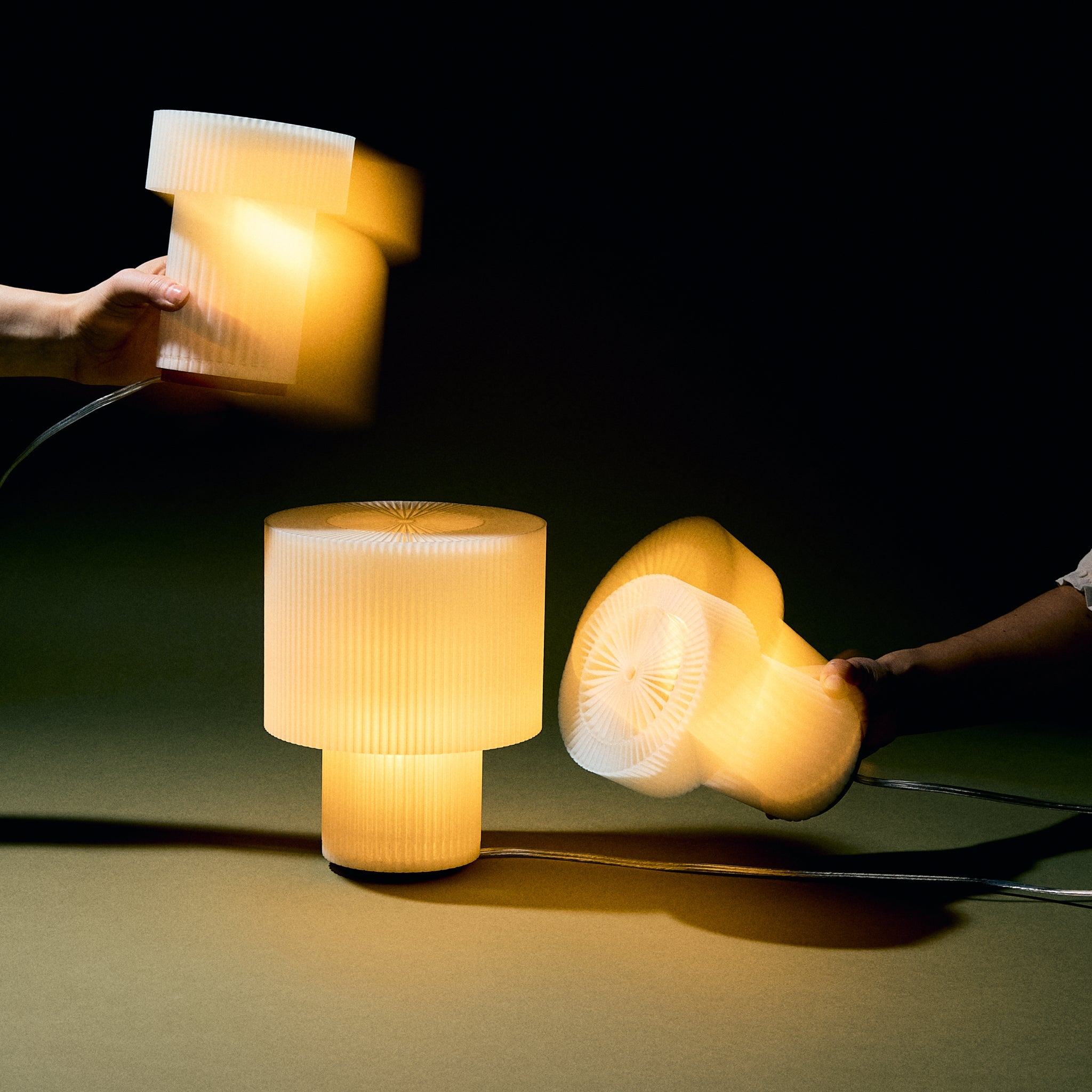 Two hands holding light-up objects next to a table lamp on a dark background