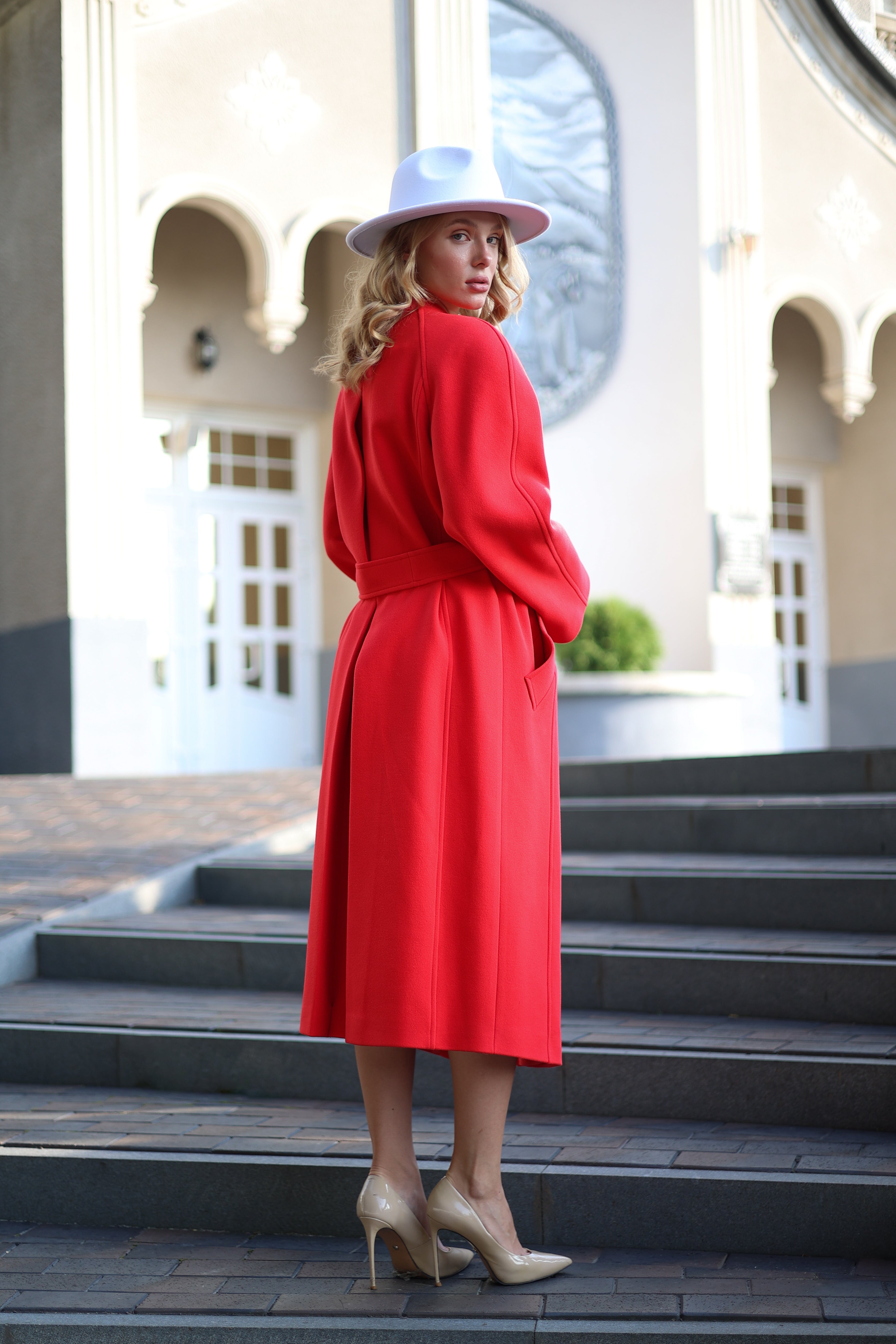 Woman in a red coat and white hat standing on steps outdoors