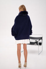 Person wearing a navy blue coat with fur collar on a white background