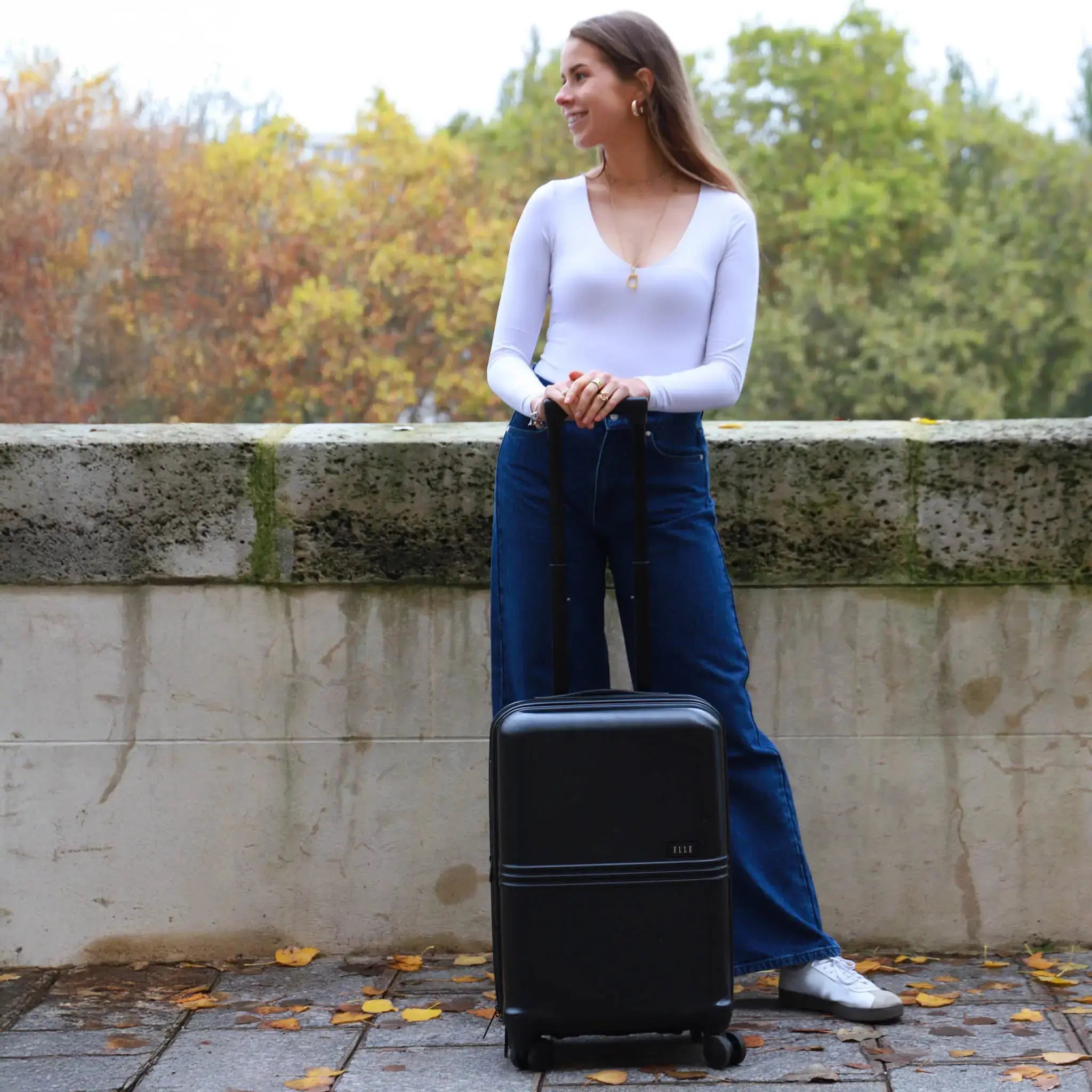 Woman standing next to a black suitcase with a scenic background