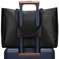 Black leather handbag with brown handle on top of a blue suitcase with brown handle