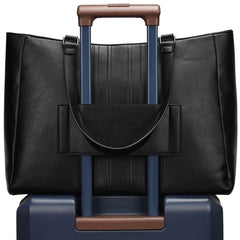 Black leather handbag with brown handle on top of a blue suitcase with brown handle