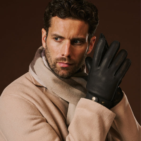 Man wearing a beige coat and black leather glove against a brown background
