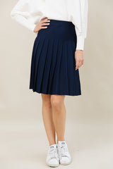Person wearing a navy pleated skirt with a white top and white sneakers on a beige background