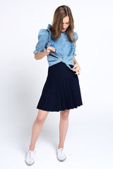 Woman wearing a blue denim shirt and navy pleated skirt on a white background