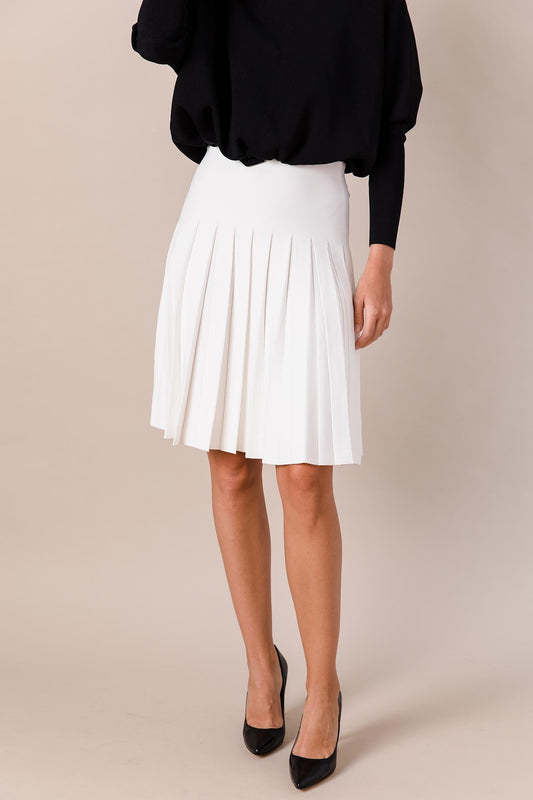 Person wearing a black top and white pleated skirt on a beige background