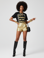 Woman wearing a black t-shirt with text, gold shorts, and black boots on a white background