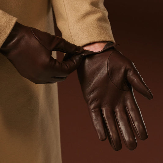 Brown leather gloves worn with a beige coat against a dark background