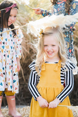 Two young girls in colorful outfits standing outdoors with straw decorations.