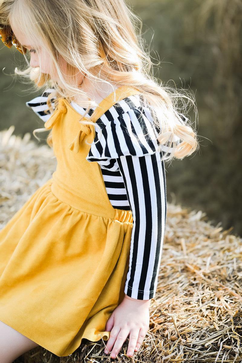 Child wearing a yellow dress over a black and white striped shirt on a natural background