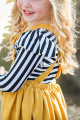 Child wearing a black and white striped shirt with yellow overalls outdoors