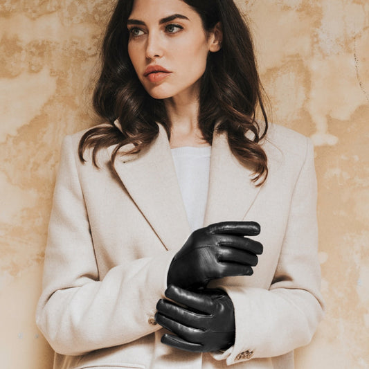 Woman wearing a beige coat and black leather gloves against a beige background
