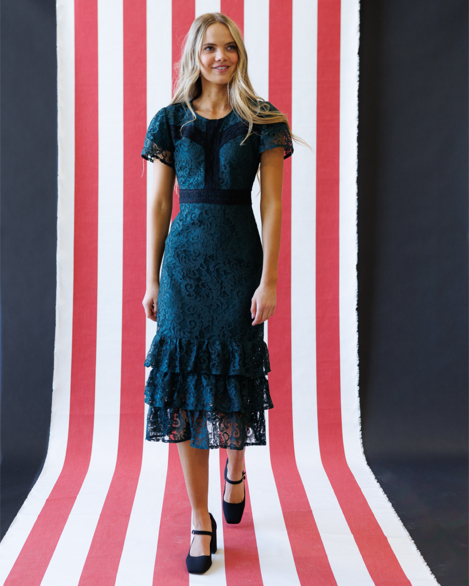 Woman wearing a dark blue lace dress standing against a red, white, and blue striped background