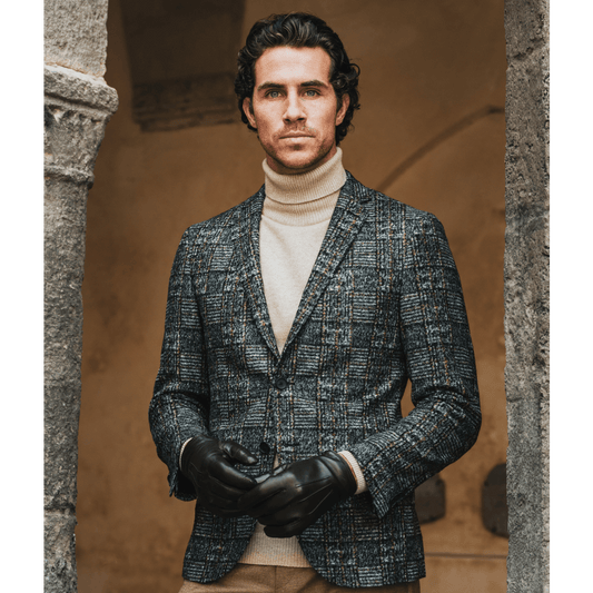 Man wearing a textured blazer and turtleneck standing against a stone wall.