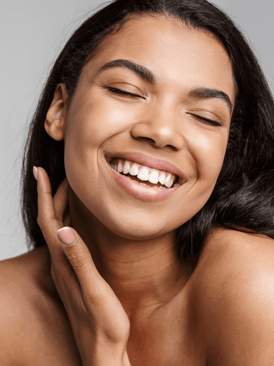 Woman with a radiant smile touching her face against a neutral background