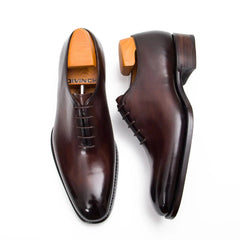 Pair of brown dress shoes with orange soles on a white background