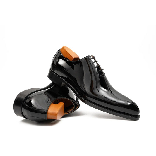 Pair of black patent leather shoes with orange soles on a white background