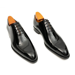 Pair of black patent leather shoes with orange tips on a white background