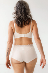 Woman wearing a white bra and high-waisted panties against a plain background