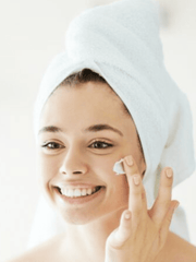 Woman applying cream to her face with a towel on her head