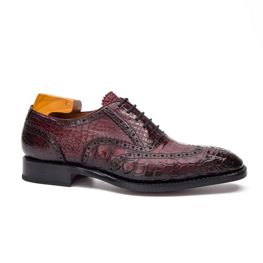 A single men's oxford dress shoe with a glossy embossed crocodile skin texture in deep burgundy and black, featuring a black sole and a bright orange shoe tree insert visible inside the collar, set against a plain white background.