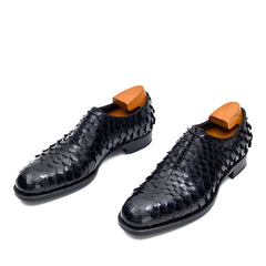 Black textured dress shoes with orange soles on a white background