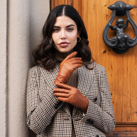 Woman wearing a checkered coat and brown gloves standing in front of a wooden door with a black knocker.