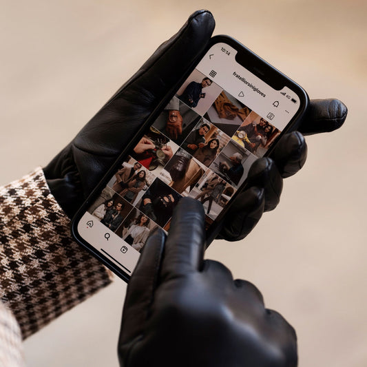 Person wearing black gloves using a smartphone with Instagram app on a beige background