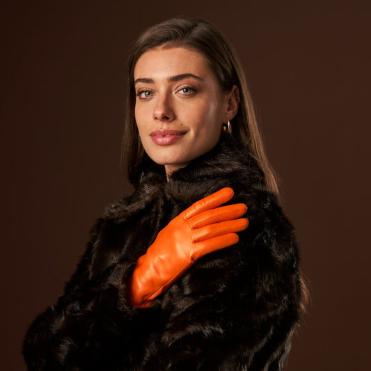 Woman wearing a black fur coat and orange gloves against a brown background