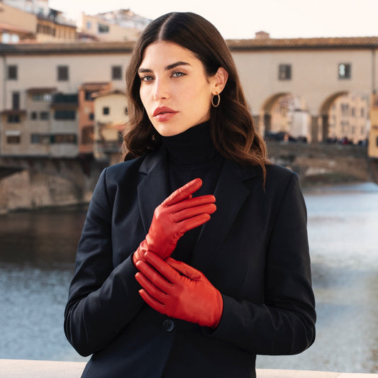 Woman wearing red gloves and a black coat with a bridge and buildings in the background