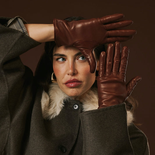 Woman wearing a brown coat with fur collar and brown leather gloves against a dark background
