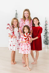 Four children in festive pajamas holding candy canes in a room with Christmas trees.