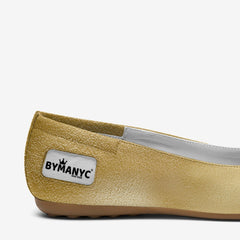Gold flat shoe with 'BYMANYC' label on a white background