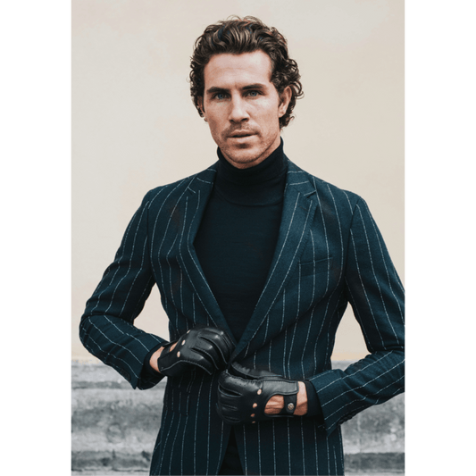 Man wearing a dark pinstripe suit and black gloves against a neutral background
